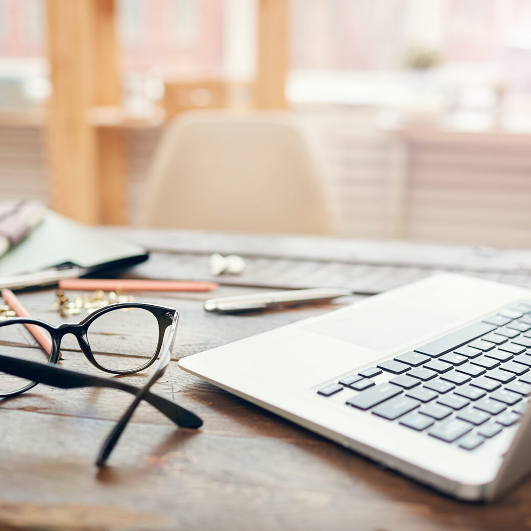 Successful Businessman Concept Background image of business office with laptop and supplies on wooden desk, focus on black hard rim glasses in foreground, copy space